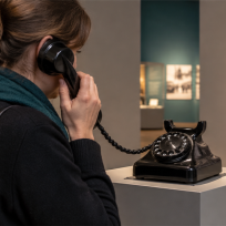 Besucherin nutzt die Telefonhörstation VINTAGE mit historischem Wählscheibentelefon im Museum